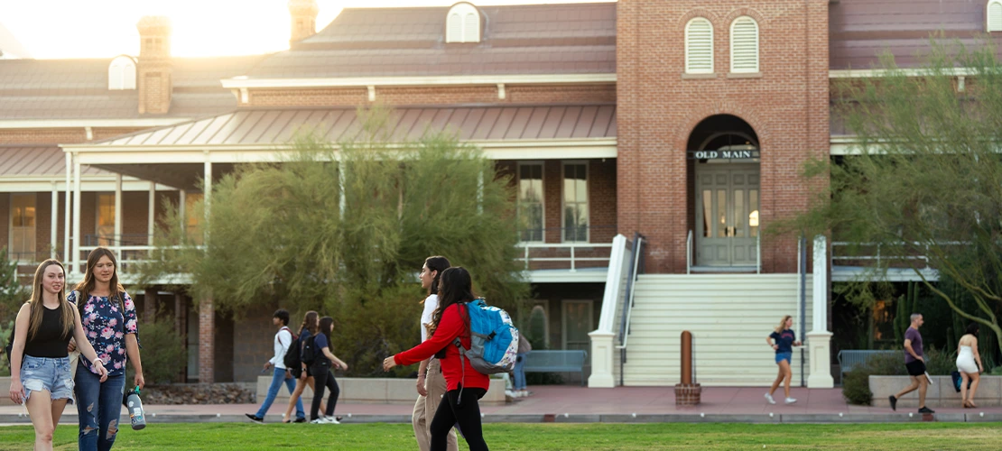 University of Arizona Old Main building at sunset with students walking in the foreground.